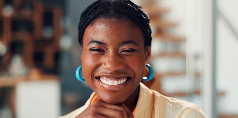 A happy woman laughing and enjoying a comfortable morning break in her living room; illustrating the proactive 'feel-good' rituals and positive attitude that help maintain long-term happiness.