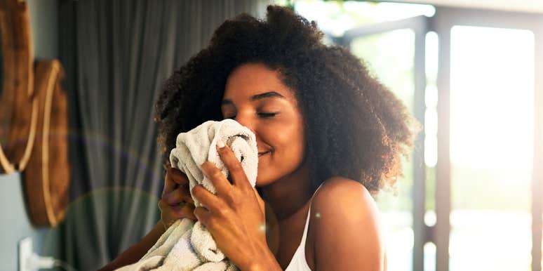 A Black female person smelling a sweater in a sunlit home; illustrating the science-backed habit of using familiar, clean domestic scents to regulate the nervous system and reduce stress.