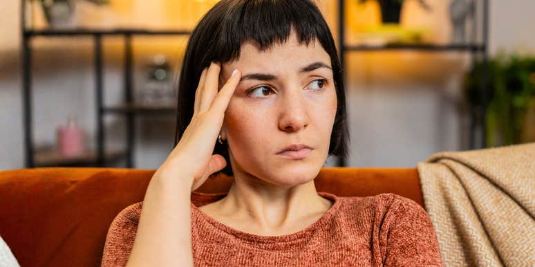 A depressed woman looking pensive and distressed while sitting alone in a living room; illustrating the internal turmoil and 'unfair situation' of a woman harboring a lie she intends to take to her grave.