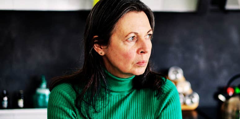 A frustrated woman looking around her kitchen; illustrating the psychological drive to control one's immediate environment through remodeling when the outside world feels increasingly unstable.