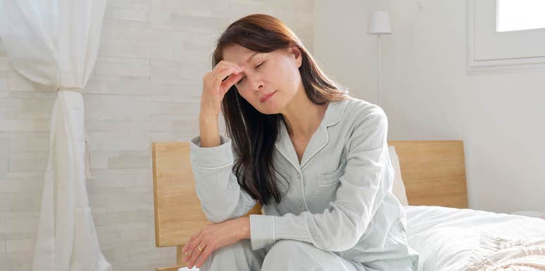 tired woman sitting on end of bed after waking up