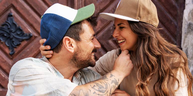 A close-up outdoor lifestyle portrait of a happy young man and woman sitting close together, sharing an authentic laugh; illustrating 'the proximity-validation matrix' where mutual humor and shared spaces catalyze romantic pairings.
