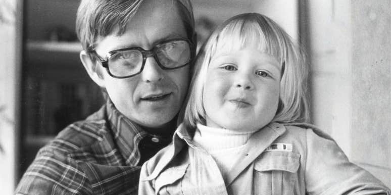 A vintage 1970s black and white photo of a father and his young daughter laughing together on wooden steps while playing with a toy boat; representing 'unplugged engagement' and the old-fashioned parenting habits that build deep emotional connections.