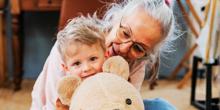 A mature grandmother holding her toddler grandson tightly in a home environment; illustrating 'the relational entitlement axis' where adult children and aging parents clash over childcare expectations.