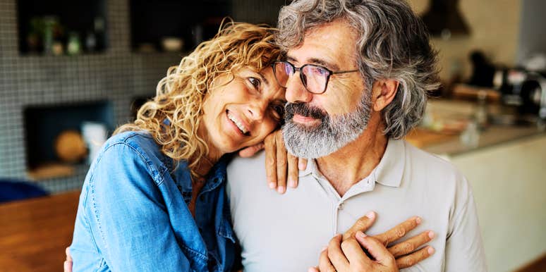 A joyful elderly husband and wife hugging tightly while looking toward the camera; illustrating 'marital longevity' and the old-fashioned conversations that preserve emotional intimacy over decades.