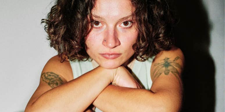 A close-up portrait of a woman with a neutral face resting on her arms; illustrating 'evolutionary signaling theory' and the non-obvious physical or behavioral traits that biological anthropologists say trigger instant social evaluations.