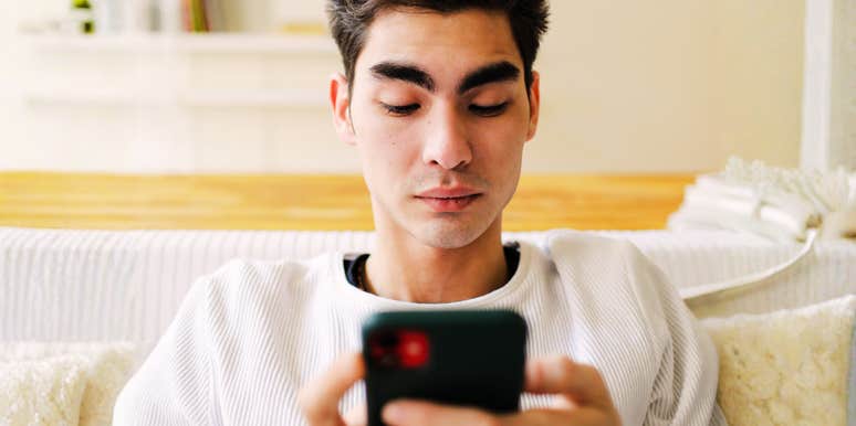 A man sitting indoors, completely absorbed as he types a message on his smartphone; a visual representation of 'textual tension' and the subtle text-ending habits that research says can make a sender come across as rude.