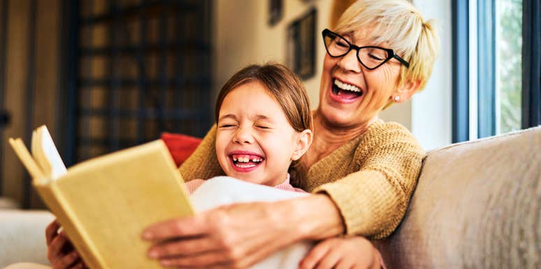 A grandma sharing a humorous moment with her grandchild over a children's storybook; illustrating 'cognitive vitality' and the spontaneous, late-life emotional healing found in intergenerational play.
