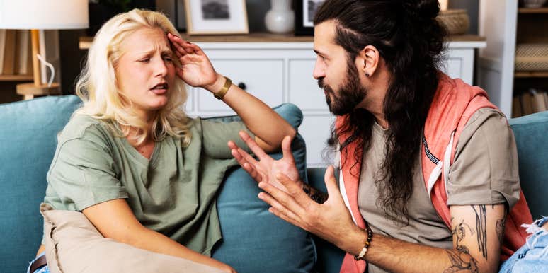 A close-up lifestyle shot of a young couple or roommates sitting in a tense posture in a home flat; illustrating 'the cognitive dissonance standoff' where a lack of internal insight leads to external blame-shifting during a dispute.