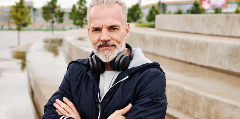 A medium portrait shot of a cheerful older gentleman in athletic clothing posing confidently outdoors at a park; illustrating 'functional longevity' and maintaining physical fitness to avoid feeling old during retirement.