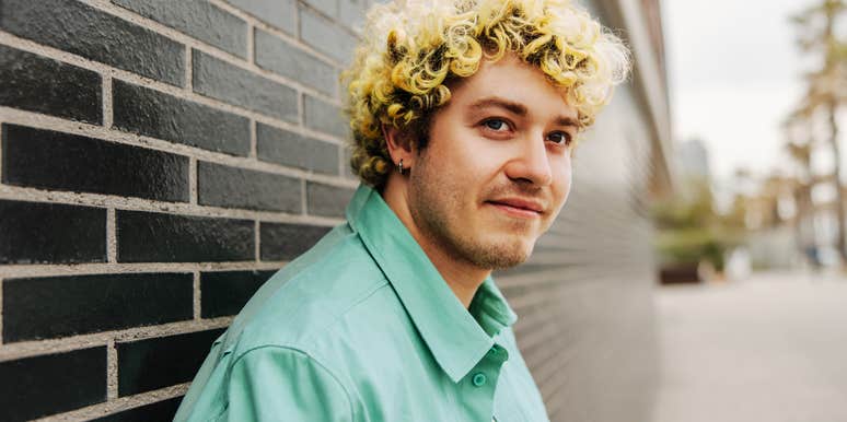 A close-up outdoor lifestyle portrait of an introspective man looking off-camera against a soft natural backdrop; illustrating 'the somatic de-escalation model' where individuals learn to process emotional triggers independently.