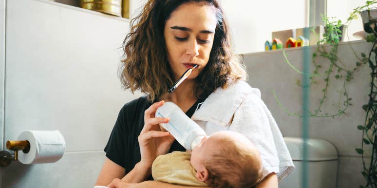 A close-up lifestyle shot of an exhausted woman managing childcare and basic personal hygiene at the same time; illustrating 'the cognitive overload conflict' where invisible household labor causes parental burnout.