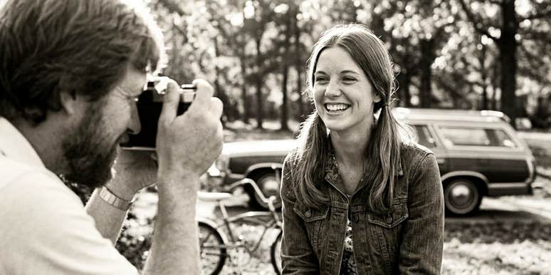 Woman laughing confidently while her partner photographs her, capturing the kind of thoughtful attention many women find meaningful in relationships