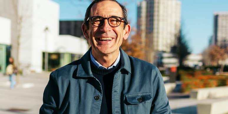 A confident mature man smiling warmly while standing in a contemporary outdoor urban space; a visual representation of 'the reclaimed director' and what daily life actually looks like two years into retirement.