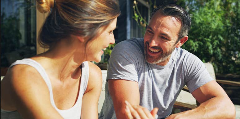An outdoor photograph of a mature husband and wife chatting comfortably on their house porch, illustrating high emotional safety, active listening, and relationship longevity.