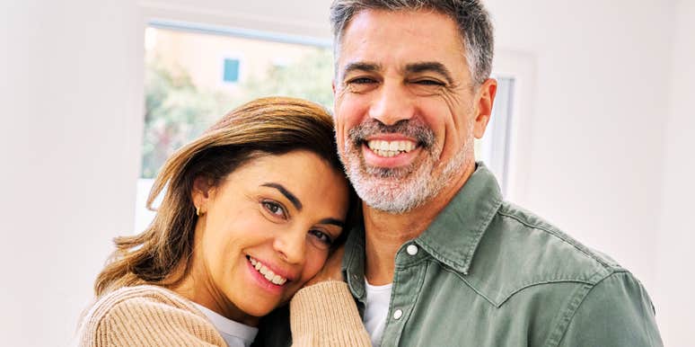 A close-up portrait of a happy, affectionate mature man and woman hugging at home and looking at the camera; illustrating 'the relational anchoring model' where classic commitment patterns survive generational shifts.