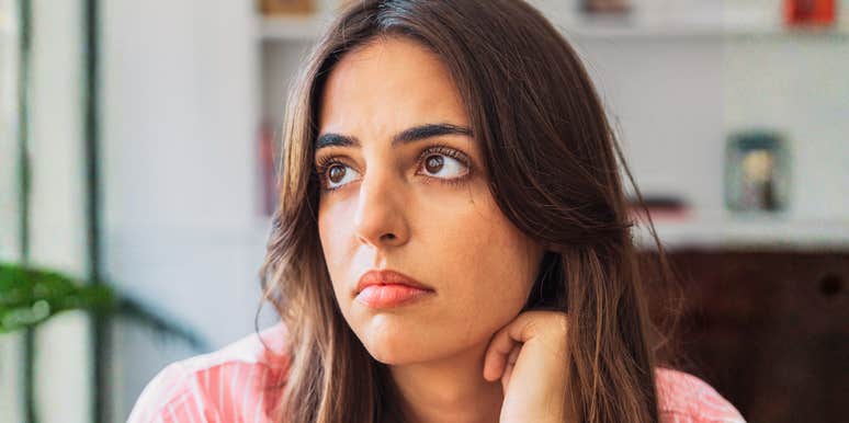 A close-up portrait of an anxious woman in deep thought, looking off-camera against a neutral backdrop; illustrating 'the institutional threat assessment model' where public safety concerns necessitate heightened individual vigilance.