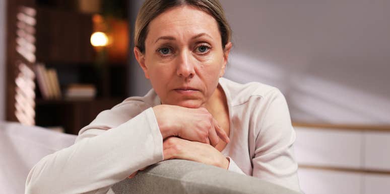 A close-up portrait of a stressed woman resting on a couch at night; illustrating 'the post-marital asset fracture' where legal agreements translate into heavy individual debt.