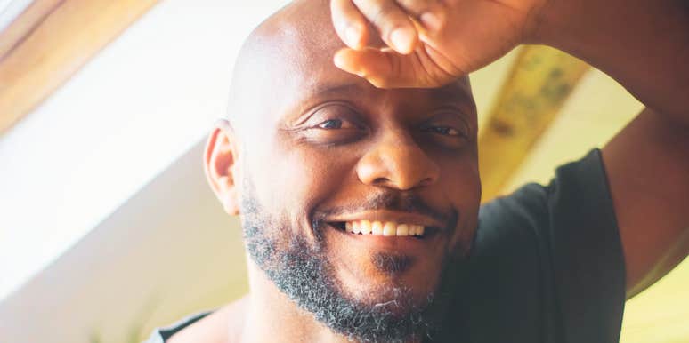 An indoor lifestyle portrait of a relaxed, happy man looking through a window with a gentle, loving smile, embodying patience, emotional intelligence, and relational satisfaction.