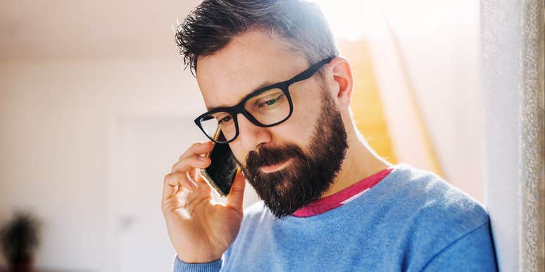 Front view of a man looking down with a tense expression while holding a smartphone in a room; illustrating 'the cognitive load of deception' archetype where body language leaks internal conflict.