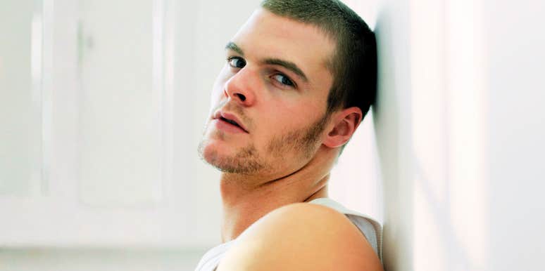 A man leaning against a plain wall with a detached expression and crossed arms, illustrating emotional distance, passive disrespect, and relational disengagement.
