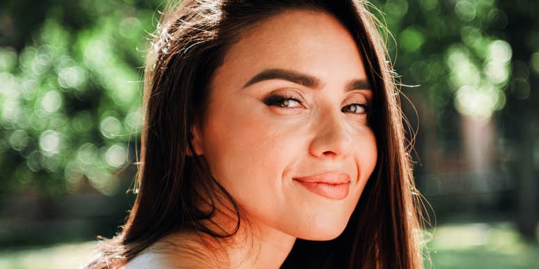 An outdoor portrait of a young woman enjoying a sunny park stroll, representing emotional safety, genuine rapport, and low-stress communication.