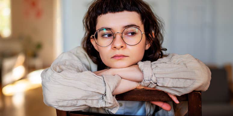 A quiet, introspective woman sitting thoughtfully by a window in her home, reflecting peace, deep focus, and self-contained emotional balance.