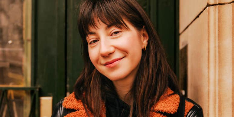A close-up portrait of a serene brunette Caucasian woman smiling gently at the camera, embodying inner peace, emotional clarity, and unforced warmth.