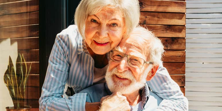 A loving elderly couple smiling and hugging outdoors in warm natural light, capturing lifestyle freedom, emotional contentment, and financial independence.