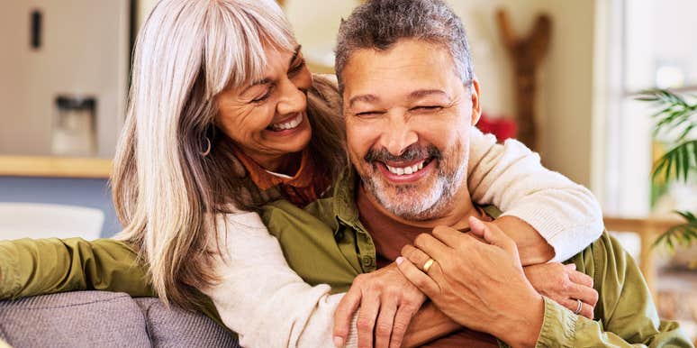 An older multiethnic couple sharing a lighthearted laugh while hugging at home, illustrating emotional resonance, lifelong intimacy, and relational attunement.