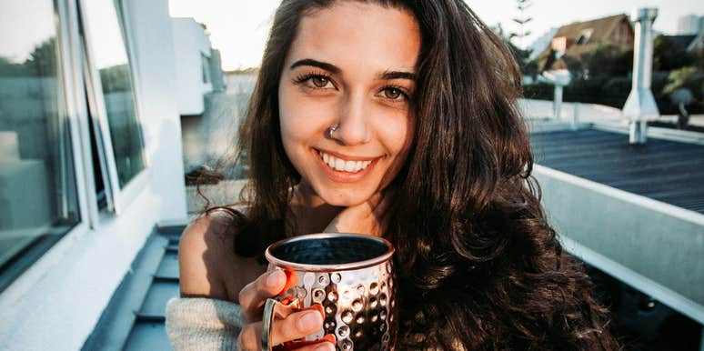 A close-up photograph of a woman smiling radiantly while enjoying a warm beverage, illustrating emotional wellbeing, security, and peaceful partnership.