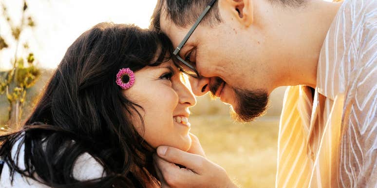 An intimate outdoor photograph of a man and woman resting their foreheads together in golden light, illustrating high emotional safety, secure attachment, and relational warmth.