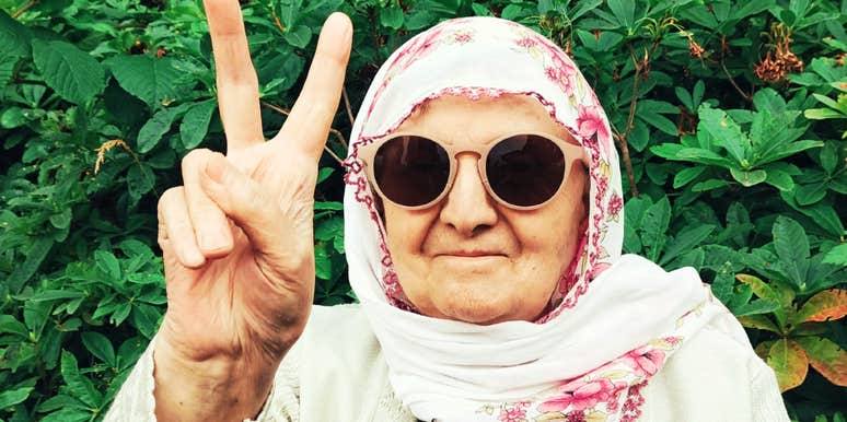 A close-up outdoor portrait of a smiling older woman with grey hair wearing modern sunglasses; illustrating 'the functional agency matrix' where late-life independence thrives.