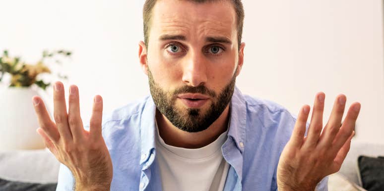 A young man with a beard making a confused gesture while sitting in a domestic setting, symbolizing communication breakdowns, low emotional intelligence, and relationship frustration.