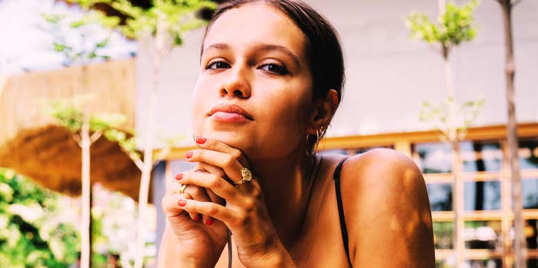 A close-up portrait of a thoughtful woman sitting at a street cafe terrace resting her chin on her hand and looking off into the distance.