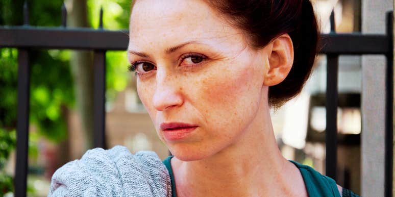 A close-up portrait of a red-haired woman with freckles looking directly at the camera with a stoic, contemplative, and somber expression.