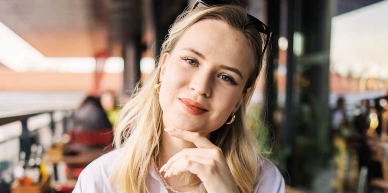 A young woman smiling thoughtfully at a city cafe terrace, symbolizing self-respect, calm inner strength, and personal autonomy.