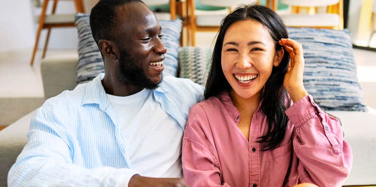 A close-up lifestyle shot of a happy couple laughing together in the sunlight, representing mutual emotional openness, warmth, and relationship satisfaction.