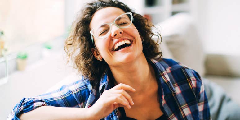 A woman relaxing on a sofa and laughing warmly, symbolizing emotional availability, natural charm, and romantic magnetics.