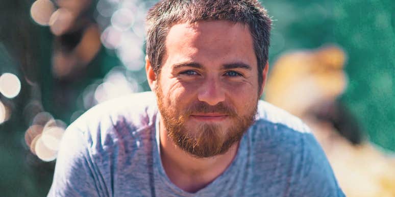 A young man with light eyes and a short beard looking into the camera outdoors near the ocean, symbolizing low-effort dating habits, emotional detachment, and casual relationships.