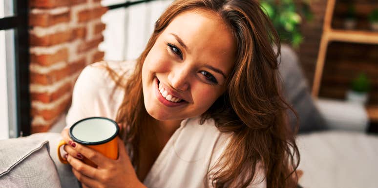 Smiling woman holds coffee mug on couch, embodying the warmth and self-awareness of people who handle forgetting a name gracefully.