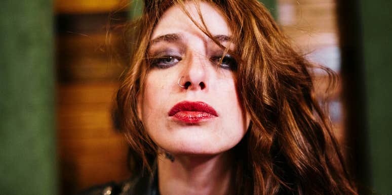 Woman with wind-swept hair and a direct gaze in a moody, editorial-style portrait.