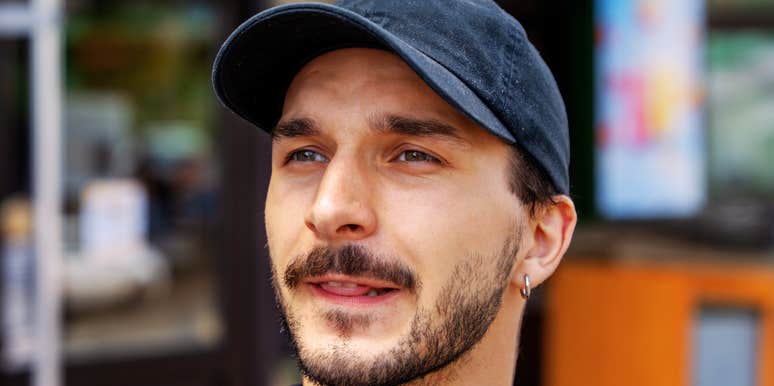 Man in a black cap and navy shirt looking off to the side with a slight smile on a city street