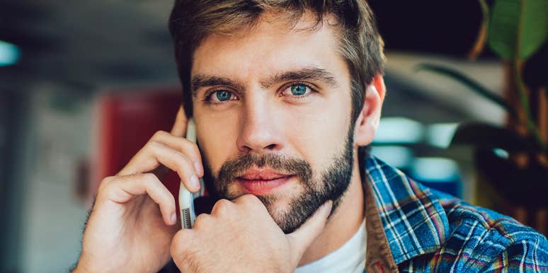 Bearded man in a plaid shirt holding a phone to his ear with his other hand at his chin, looking directly at the camera with a thoughtful expression.
