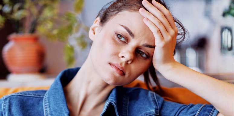 Woman in a denim jacket resting her head on her hand with a tired, worried expression
