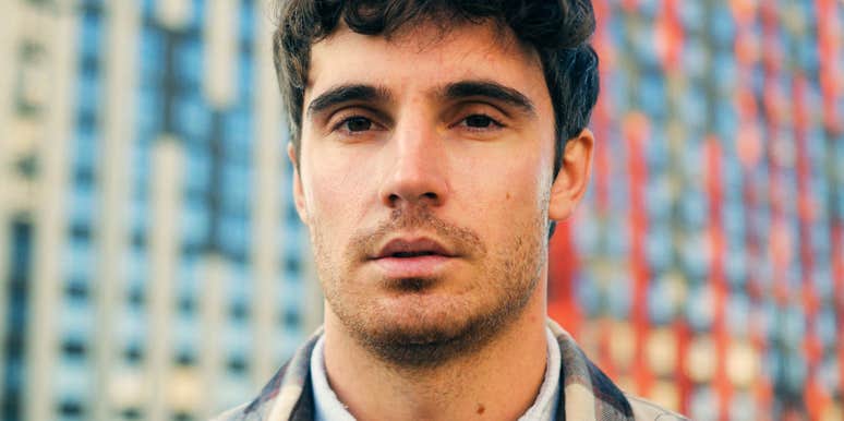 Man with dark curly hair staring intently into the camera outdoors. 