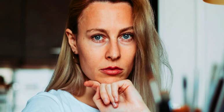 Woman with long blonde hair, serious guarded expression.
