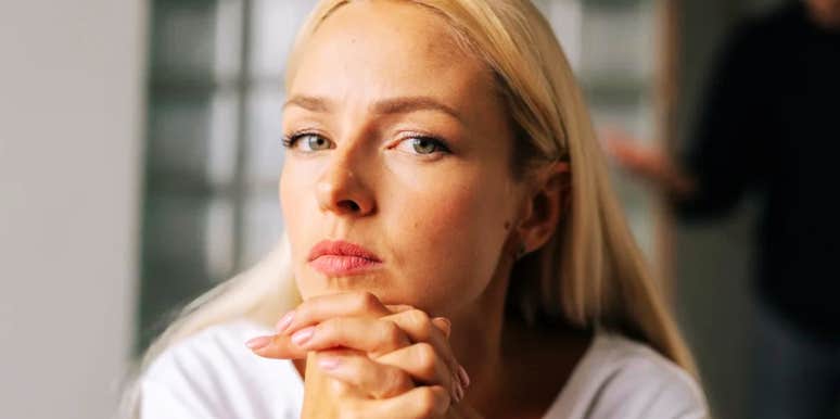 Blonde woman with hands clasped under her chin looking like she doesnt care and is not willing to compromise. 