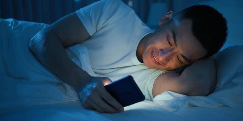 50 Sweet Good Night Messages for Him man looking at phone in dark smiling