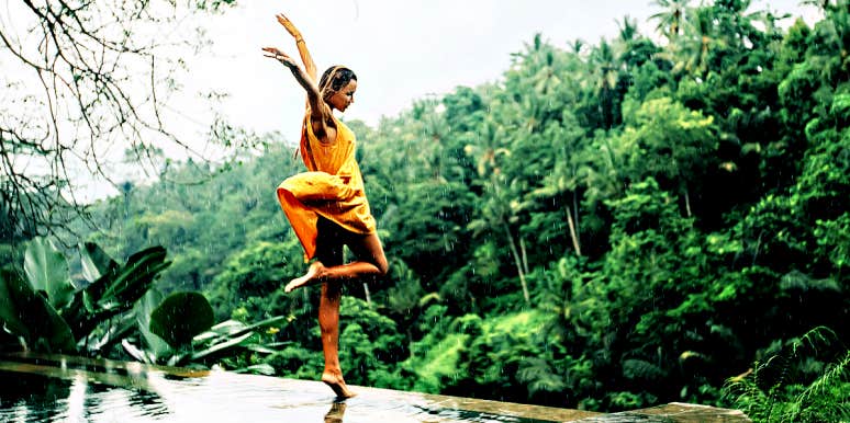 Woman in yellow dress dances in front of a jungle